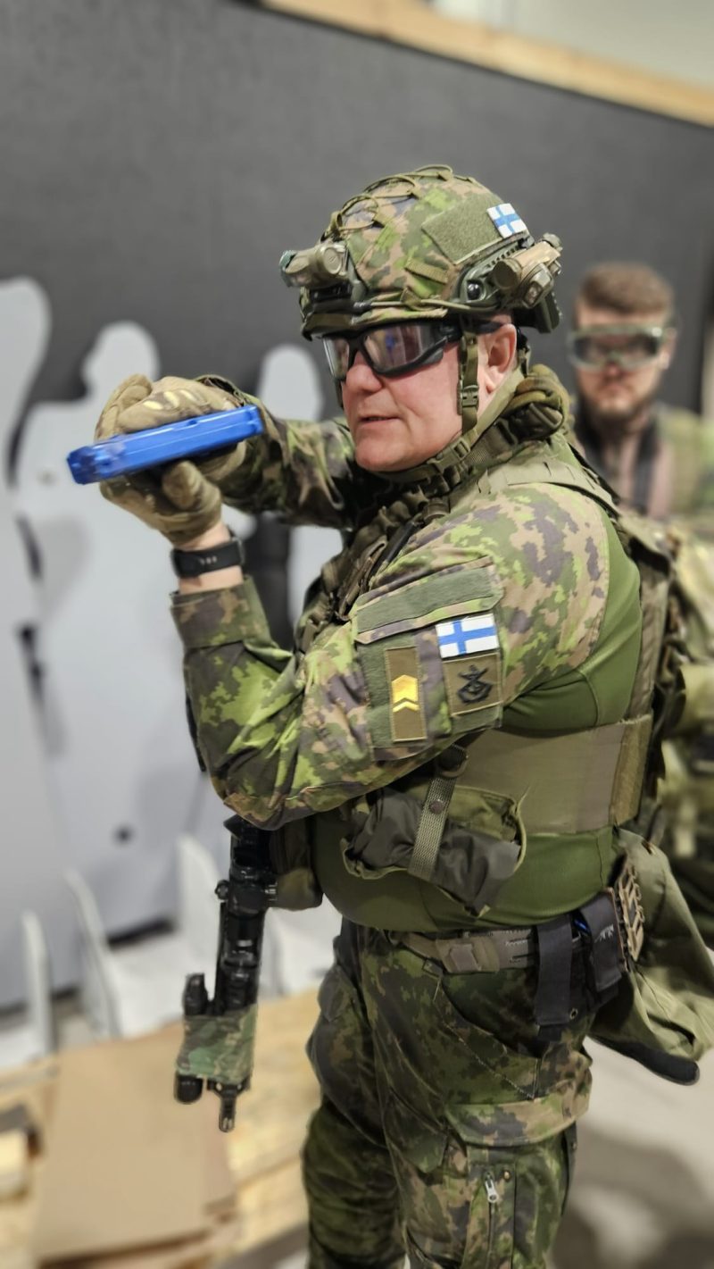 Pate demonstroi sinistä harjoituspistoolia oppilaalle Black Box -koulutustiloissa.